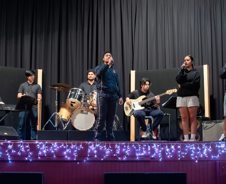 Image of students performing in an ensemble on stage with instruments and professonial lighting